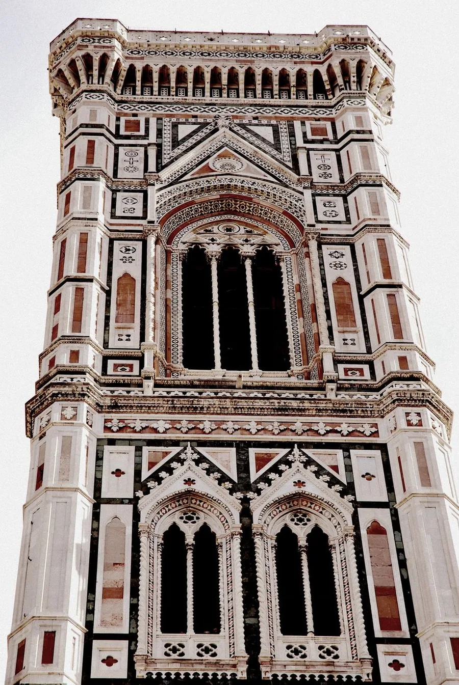 Upper levels of Giotto's Bell Tower: a tall three-light Gothic window above two paired windows, framed in white, green and pink marble beneath the corbelled top