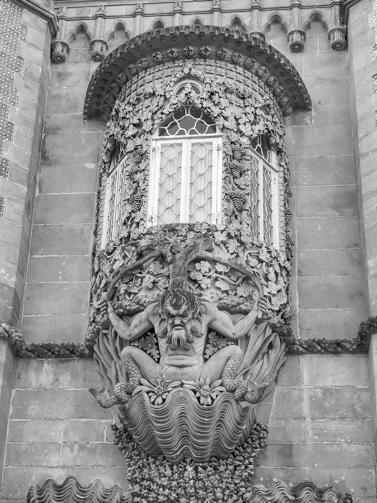 Black-and-white photo of the limestone triton crouching in a scallop shell beneath the vine-covered oriel window at Pena Palace