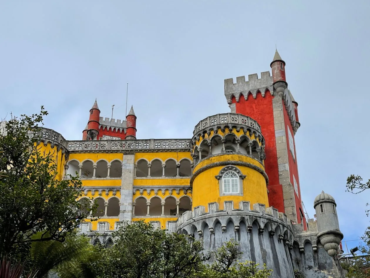 Yellow arcaded wing and red crenellated tower of Pena Palace seen from below on an overcast day