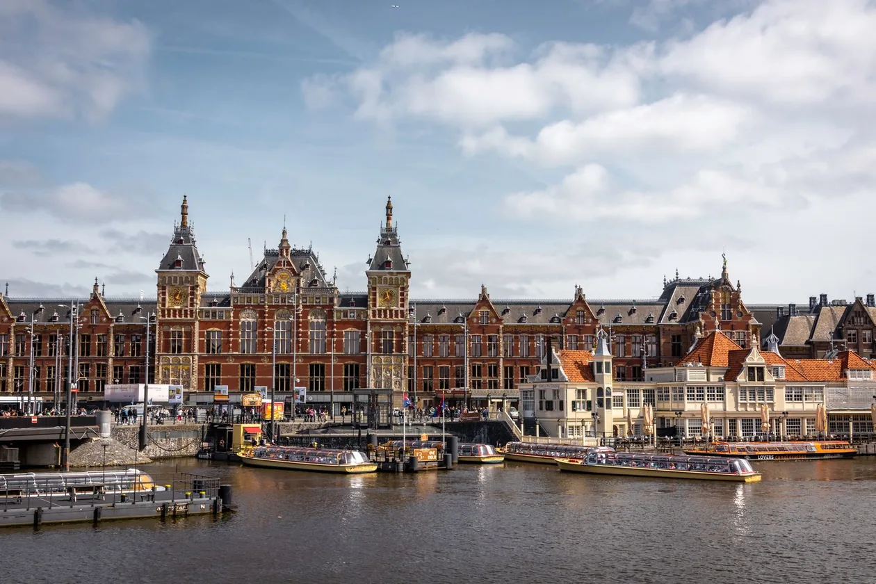 Amsterdam Centraal station seen across the water with canal cruise boats moored in front
