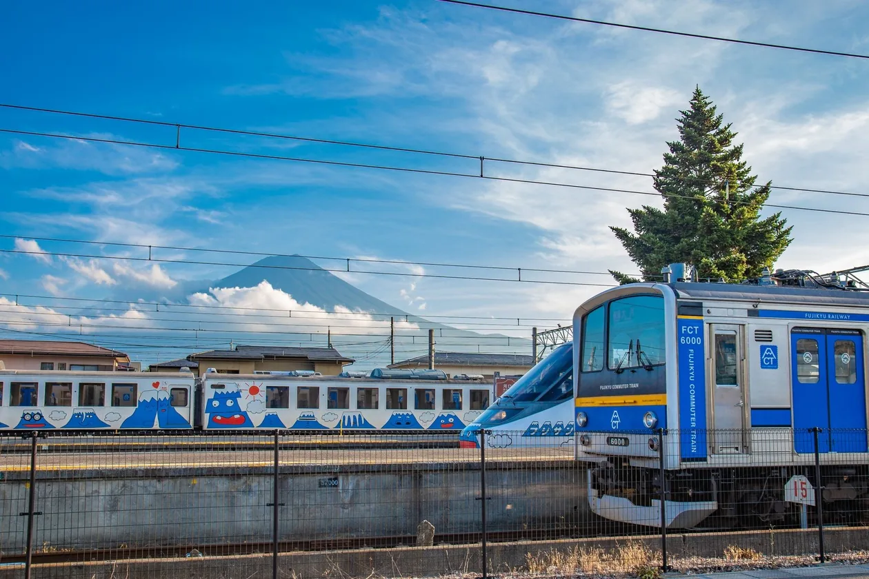Fujikyu Railway trains at a platform with Mount Fuji behind, partly covered by cloud