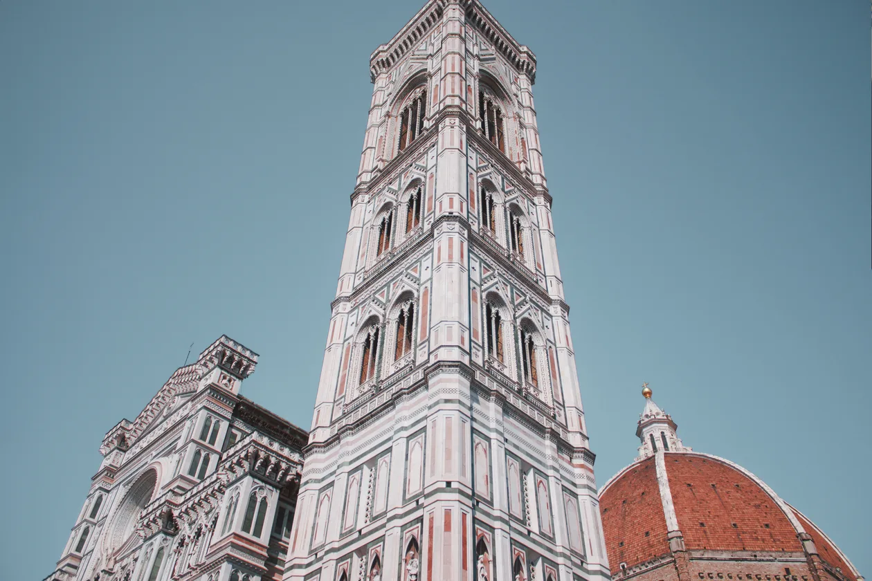 Giotto's Bell Tower seen from below in Piazza del Duomo, its white, pink and green marble rising between the cathedral facade and Brunelleschi's terracotta dome