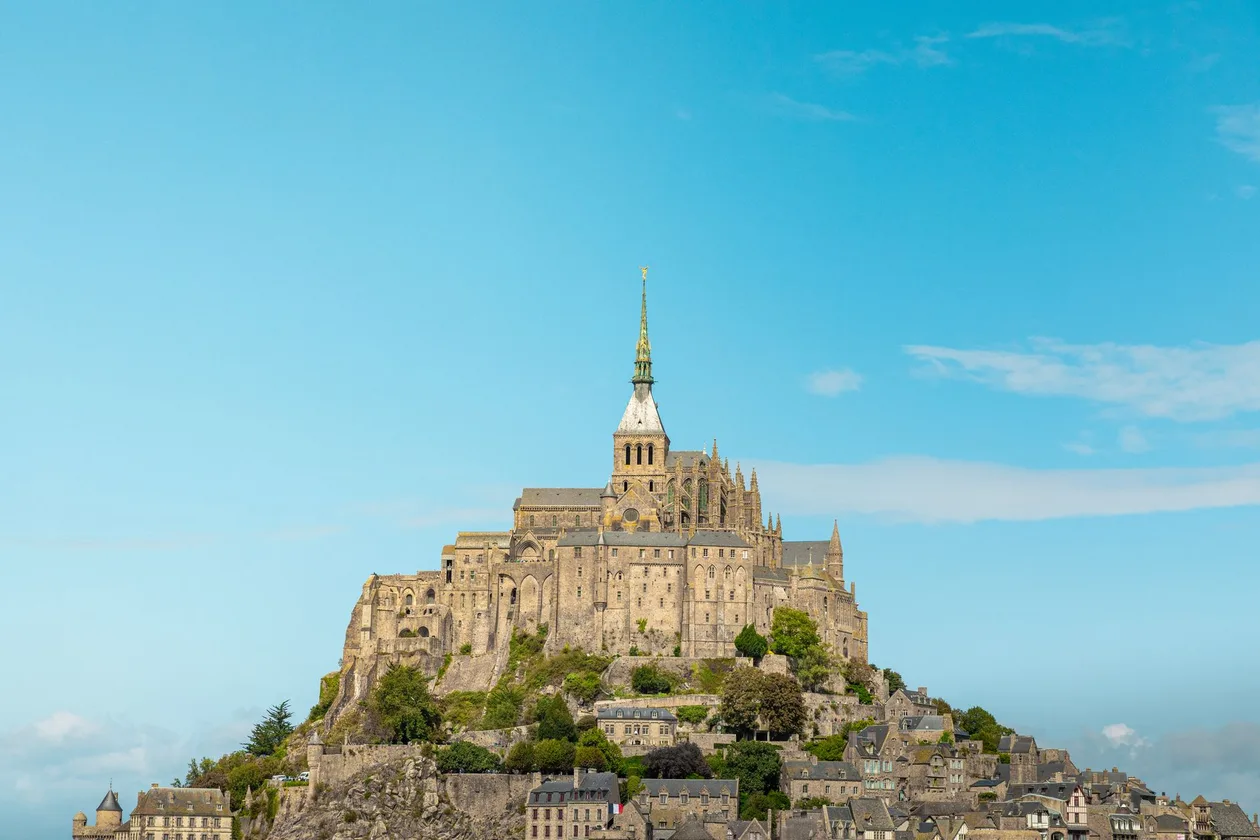 Mont-Saint-Michel seen from the bay under a clear blue sky, the abbey church and its gilded spire crowning the granite rock above the village roofs and ramparts
