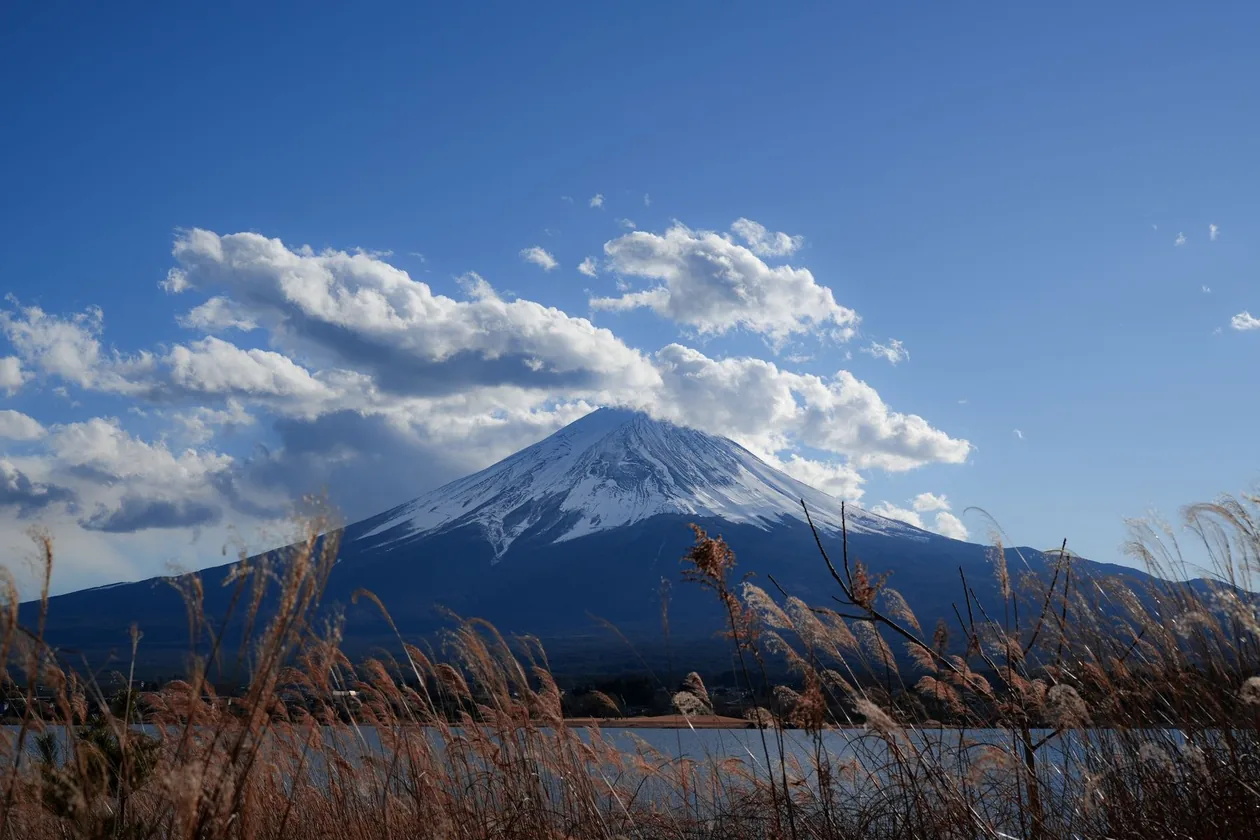 Mount Fuji seen across a lake with cloud gathering around the peak