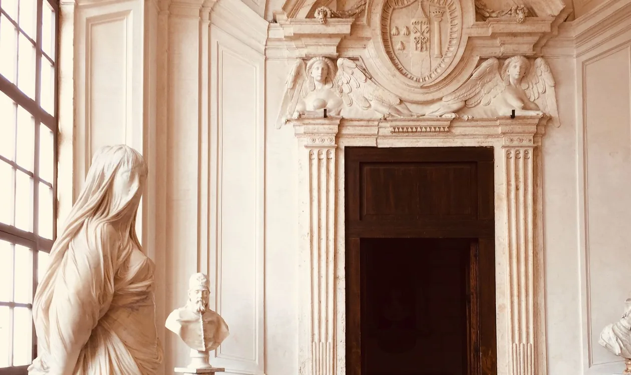 Quiet sculpture gallery at Palazzo Barberini, Rome, with a veiled marble statue beside a Baroque doorway