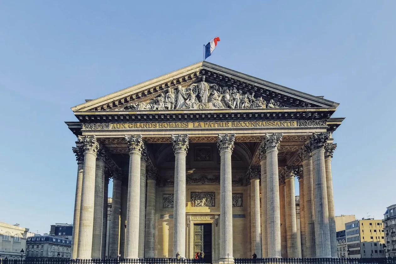 The neoclassical portico of the Panthéon in Paris seen head-on, Corinthian columns under the inscribed pediment with the French flag above