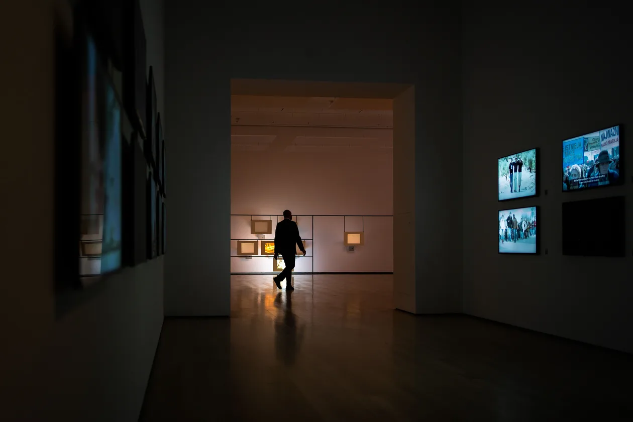 Silhouette of a visitor walking through a dark museum gallery toward a room lit by glowing video screens