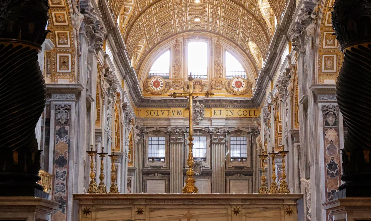 The papal altar of St Peter's Basilica seen between the twisted bronze columns of Bernini's Baldachin, with the gilded barrel vault and the nave inscription above