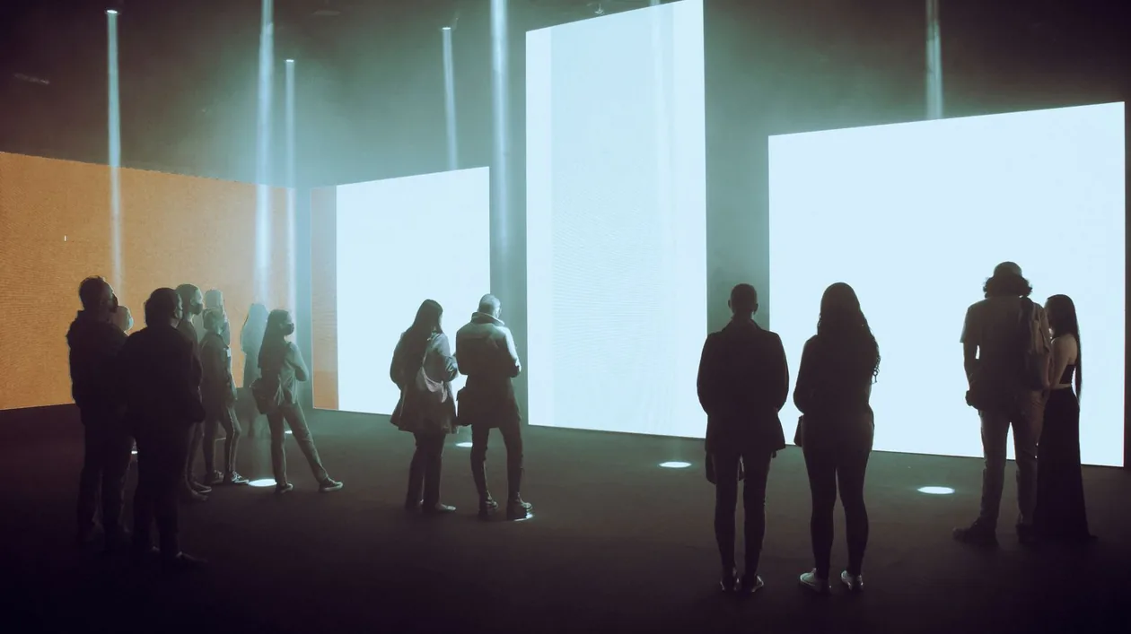 Visitors as silhouettes inside an immersive digital art exhibition with illuminated screens
